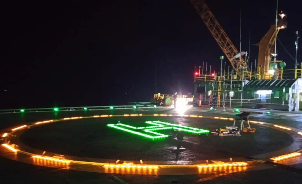 Illuminated helideck with green H marking and perimeter lighting at night